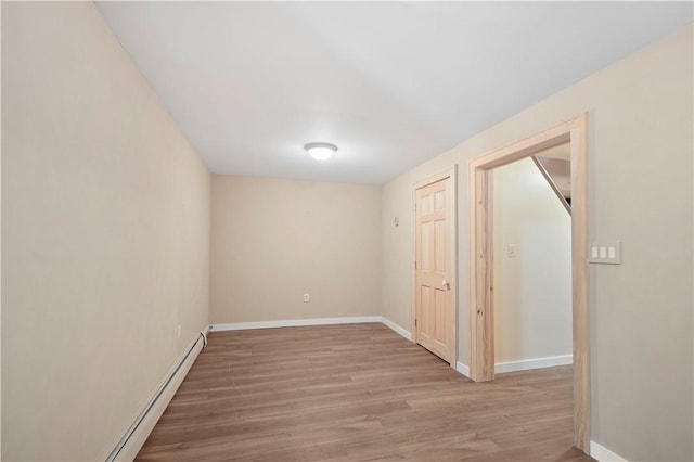 spare room featuring light wood finished floors, a baseboard heating unit, and baseboards