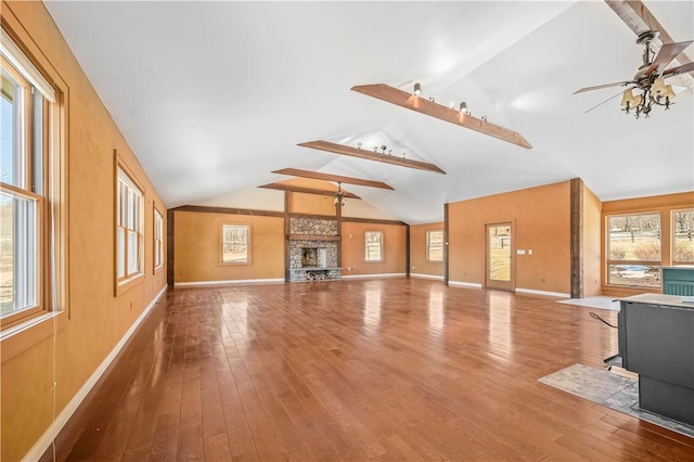 unfurnished living room with baseboards, vaulted ceiling, a wood stove, wood finished floors, and a ceiling fan