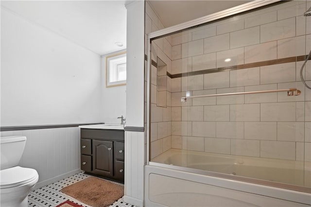 full bathroom featuring wainscoting, toilet, vanity, and bath / shower combo with glass door