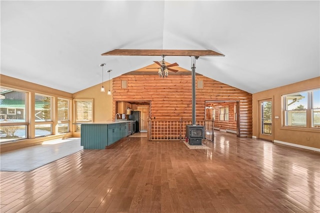 unfurnished living room with ceiling fan, beam ceiling, hardwood / wood-style floors, and a wood stove