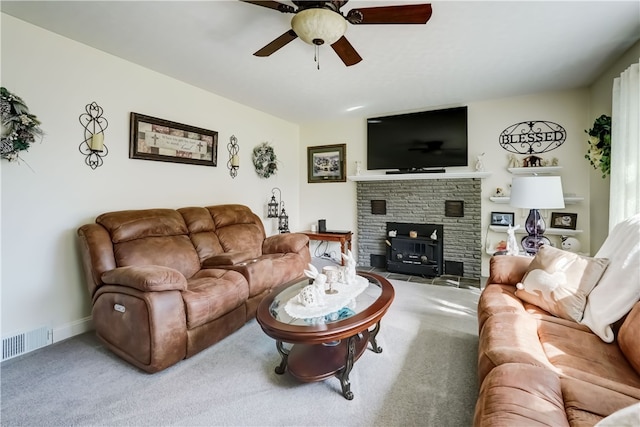 carpeted living room with baseboards, visible vents, a stone fireplace, and ceiling fan