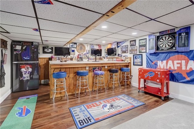 bar featuring indoor wet bar, freestanding refrigerator, baseboards, and wood finished floors