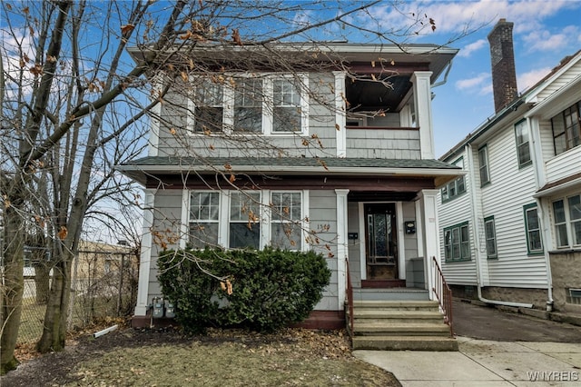 view of front of property with entry steps, a balcony, and fence