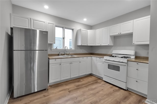 kitchen featuring white range with gas cooktop, a sink, white cabinetry, freestanding refrigerator, and light wood finished floors