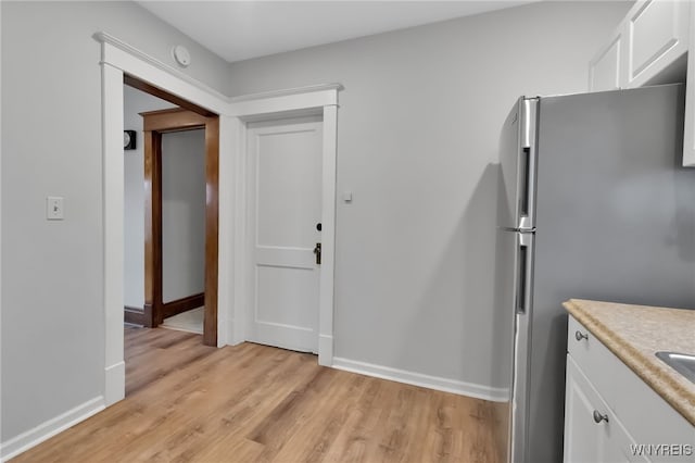 kitchen with light wood-type flooring, freestanding refrigerator, white cabinetry, light countertops, and baseboards