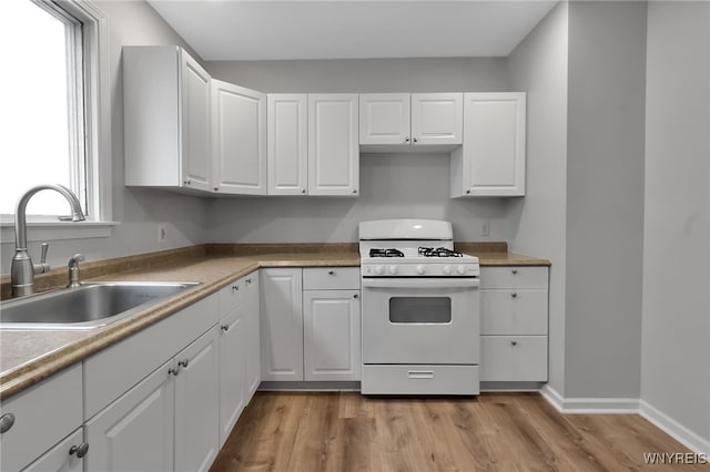 kitchen featuring baseboards, white range with gas cooktop, a sink, white cabinets, and light wood-type flooring