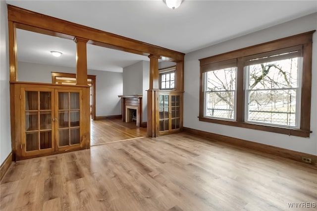 empty room featuring decorative columns, baseboards, and light wood finished floors