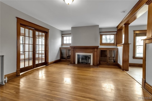 unfurnished living room with a fireplace with flush hearth, light wood-type flooring, and baseboards