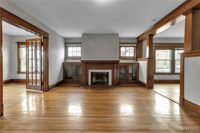 unfurnished living room with a fireplace with flush hearth, light wood-style floors, and baseboards