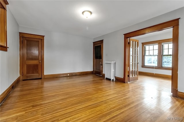 unfurnished room featuring light wood-style flooring, radiator, and baseboards