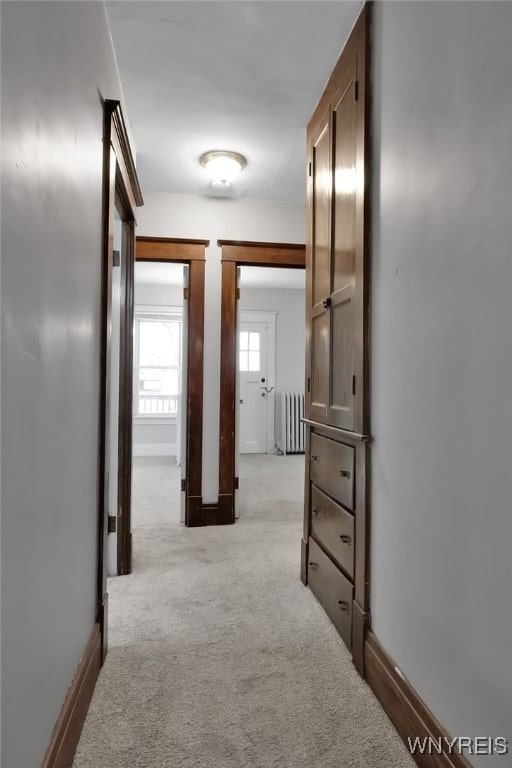 corridor featuring radiator, light colored carpet, and baseboards