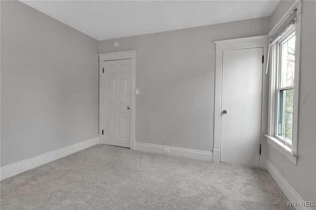 unfurnished bedroom featuring baseboards, multiple windows, and light carpet