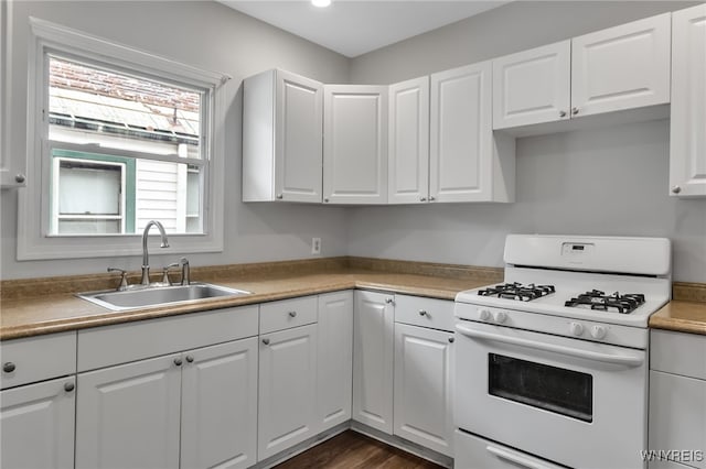 kitchen featuring a sink, gas range gas stove, dark wood-type flooring, and white cabinets