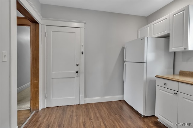 kitchen featuring baseboards, freestanding refrigerator, dark wood-type flooring, light countertops, and white cabinetry