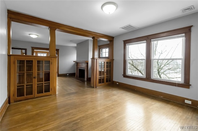 empty room with decorative columns, visible vents, light wood-type flooring, and baseboards