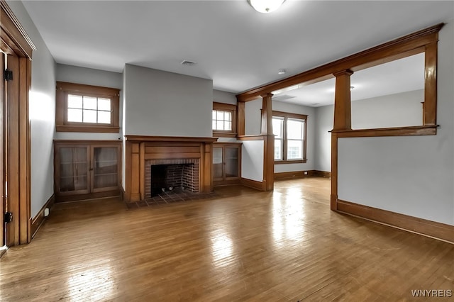 unfurnished living room with visible vents, baseboards, a brick fireplace, and hardwood / wood-style flooring