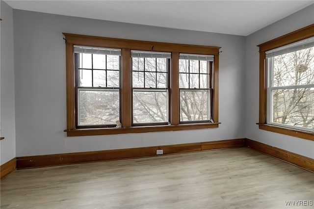 empty room featuring a healthy amount of sunlight, light wood-style flooring, and baseboards