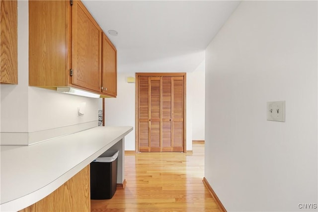 kitchen featuring brown cabinets, light countertops, light wood-type flooring, and baseboards