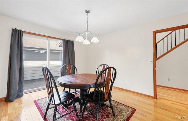 dining room featuring baseboards, light wood-style floors, an inviting chandelier, and stairs