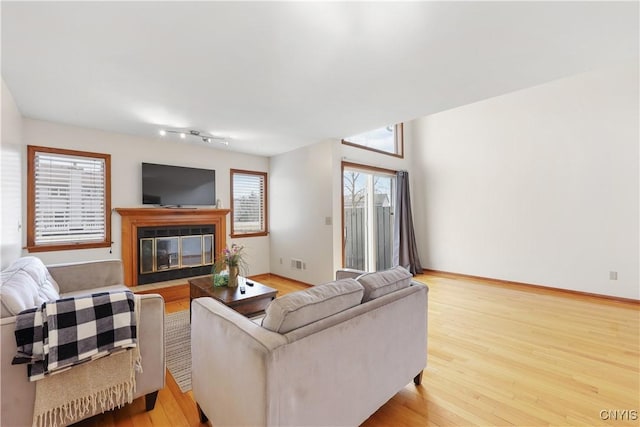 living room with visible vents, baseboards, a glass covered fireplace, and wood finished floors