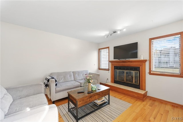 living room featuring a glass covered fireplace, baseboards, and light wood-style flooring