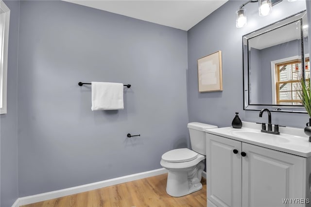 half bath with toilet, vanity, baseboards, and wood finished floors