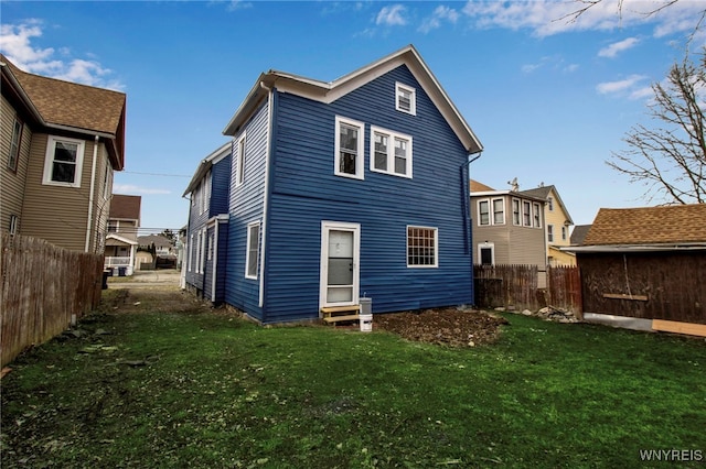 rear view of property with entry steps, a yard, and fence