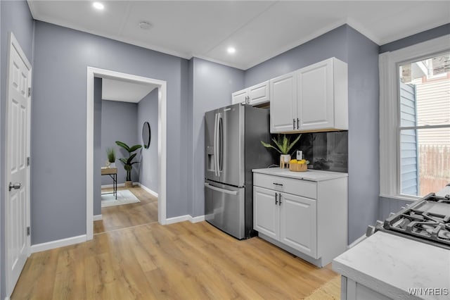 kitchen with light wood finished floors, stainless steel fridge, white cabinets, and ornamental molding