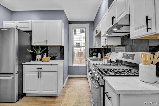 kitchen with baseboards, under cabinet range hood, light wood-style flooring, appliances with stainless steel finishes, and white cabinetry