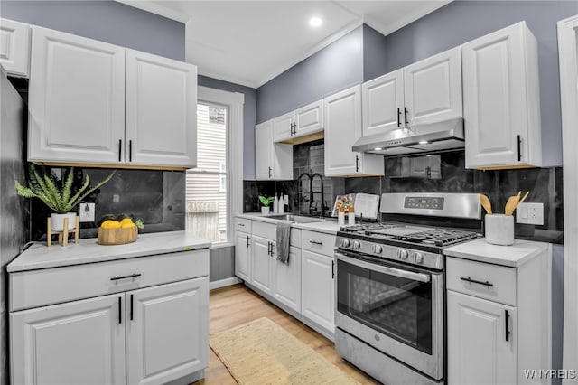 kitchen featuring under cabinet range hood, gas range, light countertops, and a sink