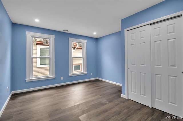 unfurnished bedroom with visible vents, baseboards, a closet, and dark wood-style floors