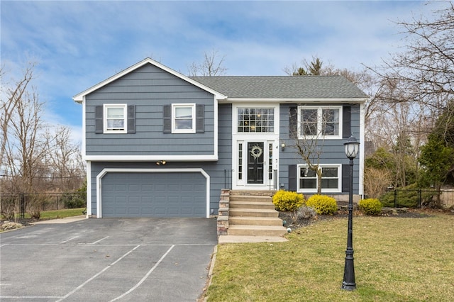 split foyer home with fence, driveway, an attached garage, a shingled roof, and a front lawn