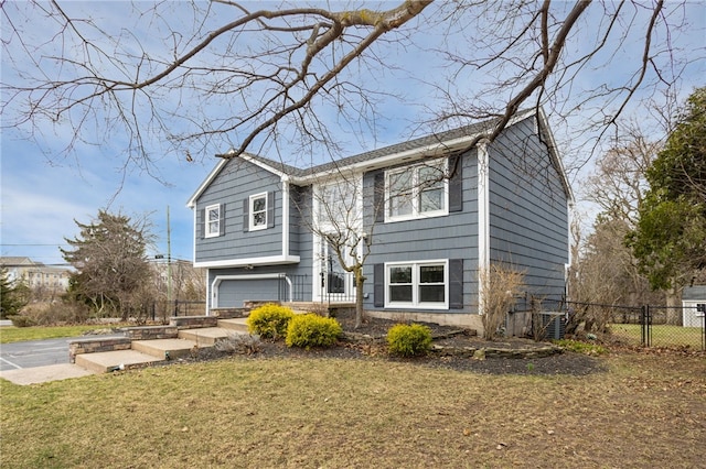 bi-level home featuring a garage, driveway, a front lawn, and fence