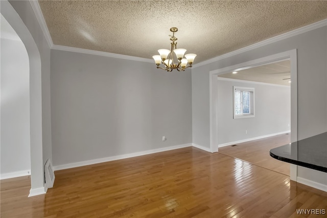 unfurnished dining area with wood finished floors, arched walkways, ornamental molding, a textured ceiling, and a chandelier