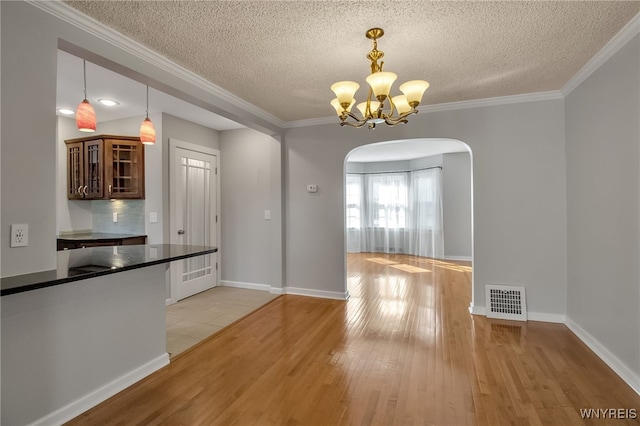 unfurnished dining area featuring visible vents, an inviting chandelier, light wood-style flooring, arched walkways, and ornamental molding