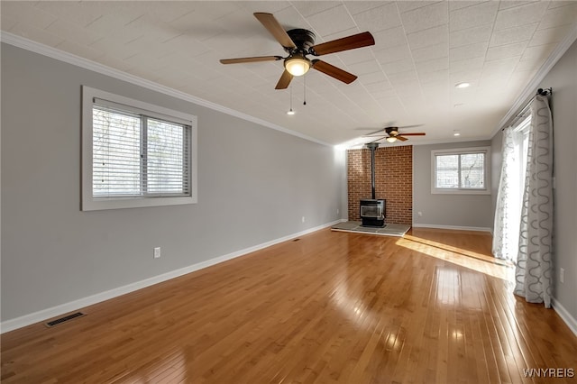 unfurnished living room with a wood stove, a ceiling fan, visible vents, and ornamental molding