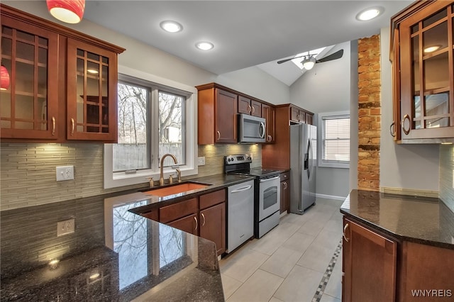 kitchen featuring backsplash, dark stone counters, stainless steel appliances, a ceiling fan, and a sink