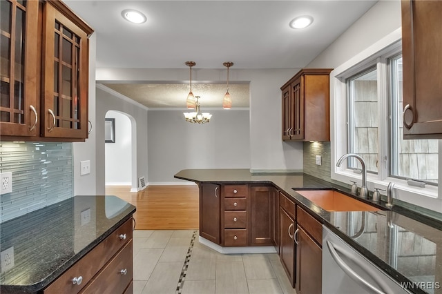 kitchen with dark stone counters, arched walkways, a sink, stainless steel dishwasher, and a notable chandelier