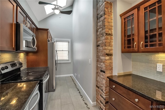 kitchen featuring lofted ceiling with skylight, stainless steel appliances, dark stone counters, glass insert cabinets, and ceiling fan