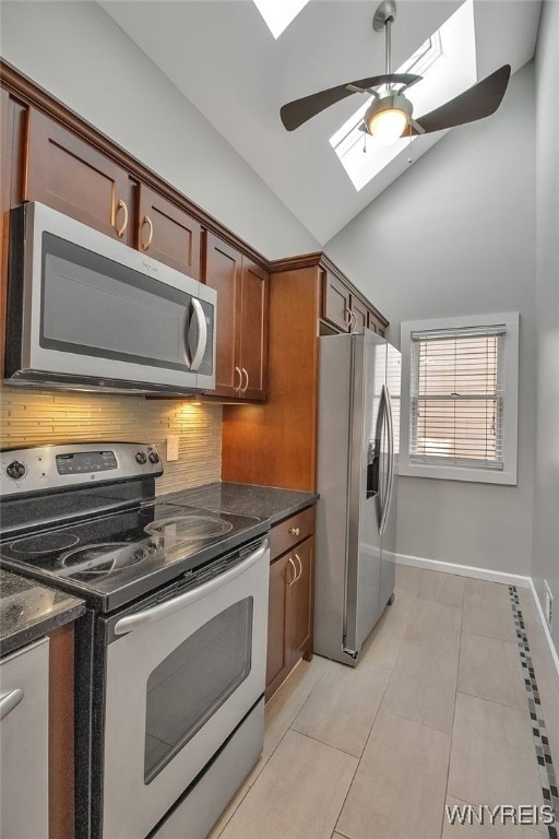 kitchen featuring tasteful backsplash, vaulted ceiling with skylight, appliances with stainless steel finishes, dark stone countertops, and a ceiling fan