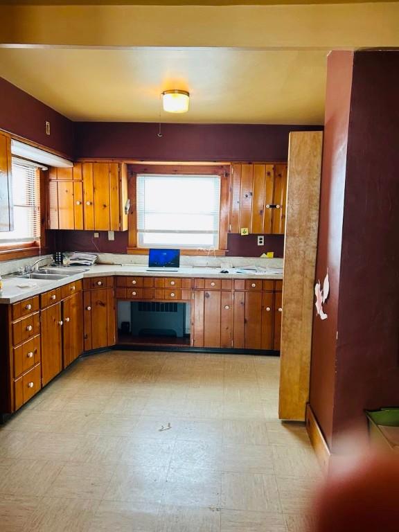 kitchen with a sink, plenty of natural light, brown cabinetry, light countertops, and light floors