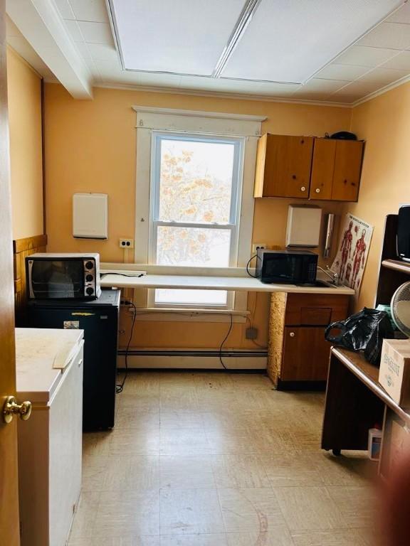 kitchen with a baseboard radiator, brown cabinets, black microwave, and light countertops