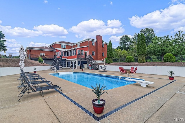 pool with a diving board, fence, stairs, and a patio area