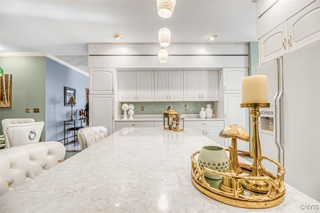 kitchen featuring light stone countertops, white cabinetry, white refrigerator with ice dispenser, and ornamental molding