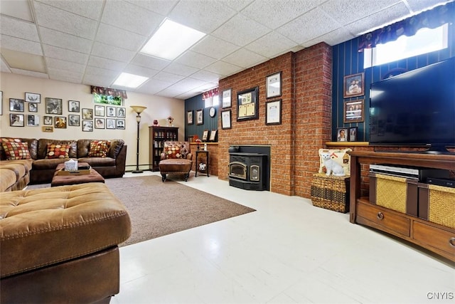living area with tile patterned floors, a paneled ceiling, brick wall, and a wood stove