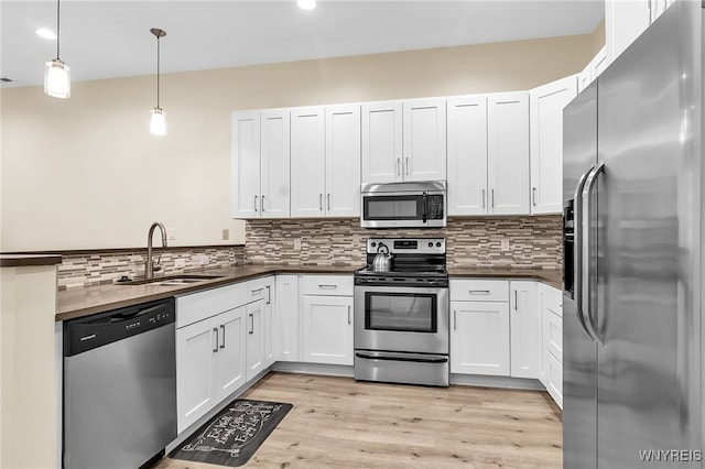 kitchen featuring dark countertops, decorative backsplash, light wood-style flooring, stainless steel appliances, and a sink
