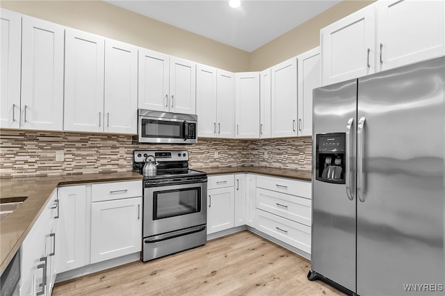 kitchen featuring light wood-type flooring, stainless steel appliances, dark countertops, and decorative backsplash