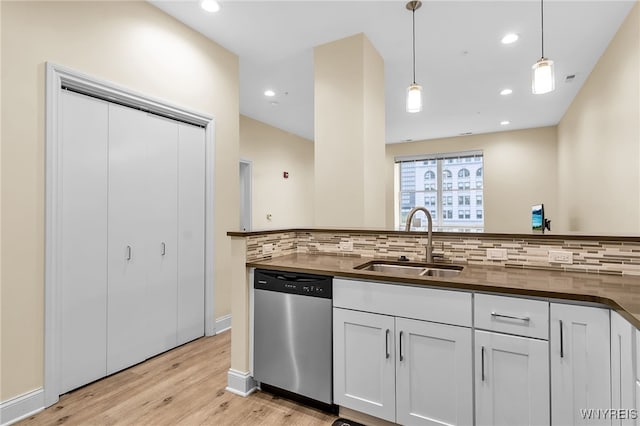 kitchen featuring light wood finished floors, pendant lighting, decorative backsplash, stainless steel dishwasher, and a sink