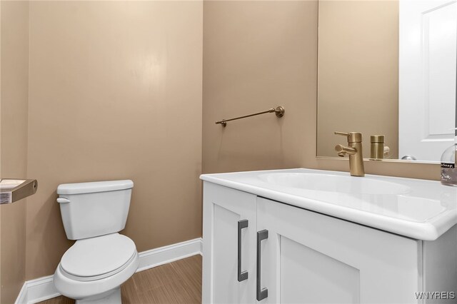 half bath featuring toilet, vanity, and baseboards