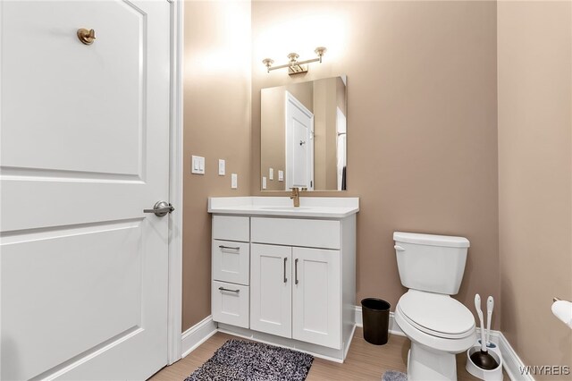 bathroom featuring baseboards, toilet, wood finished floors, and vanity
